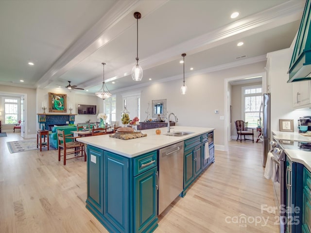 kitchen featuring sink, light hardwood / wood-style flooring, appliances with stainless steel finishes, hanging light fixtures, and a center island with sink