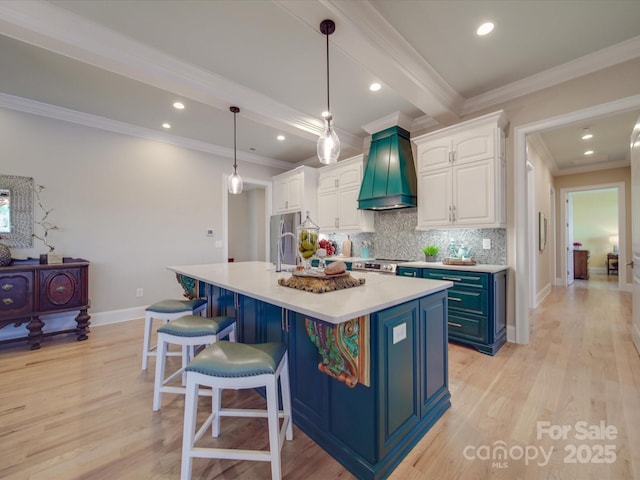 kitchen featuring premium range hood, pendant lighting, white cabinets, a kitchen island with sink, and light hardwood / wood-style floors