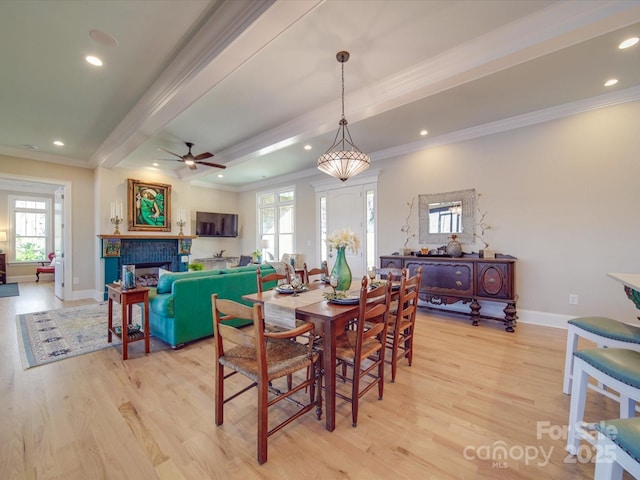 dining room with beam ceiling, crown molding, light hardwood / wood-style flooring, ceiling fan, and a fireplace