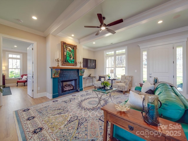 living room featuring a tile fireplace, beamed ceiling, ceiling fan, crown molding, and light wood-type flooring