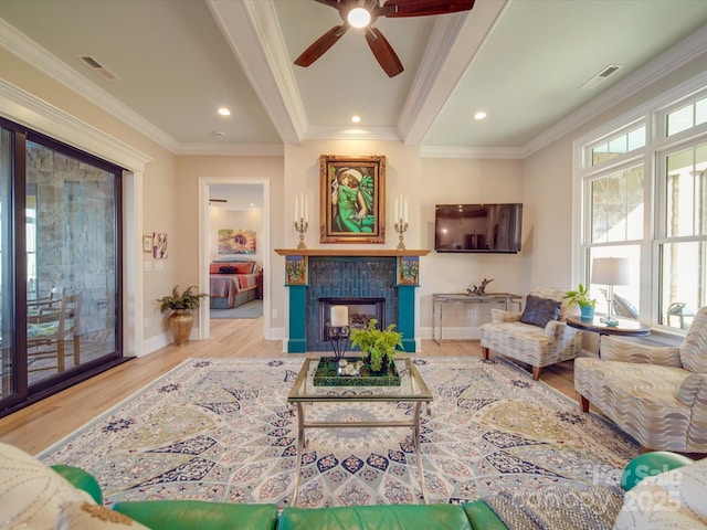 living room with crown molding, ceiling fan, a fireplace, and light wood-type flooring