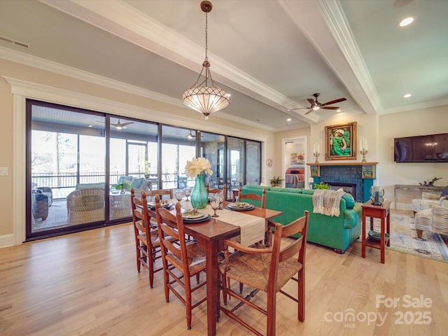 dining area with a tiled fireplace, ornamental molding, ceiling fan, and light hardwood / wood-style flooring