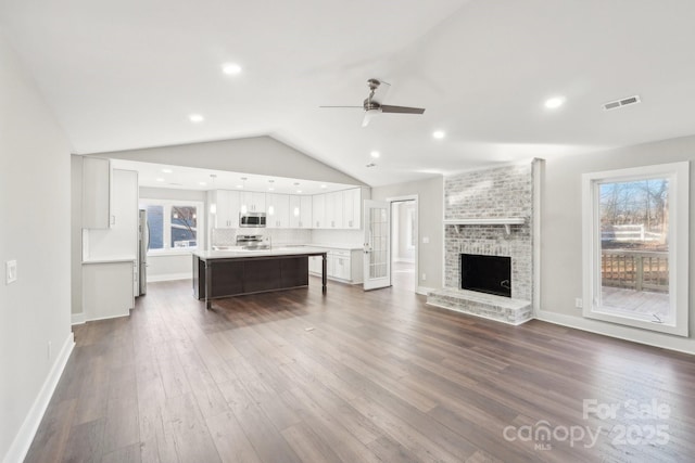 unfurnished living room with dark hardwood / wood-style floors, vaulted ceiling, a brick fireplace, and a wealth of natural light