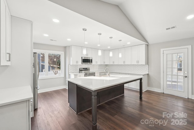 kitchen with white cabinetry, hanging light fixtures, backsplash, stainless steel appliances, and an island with sink