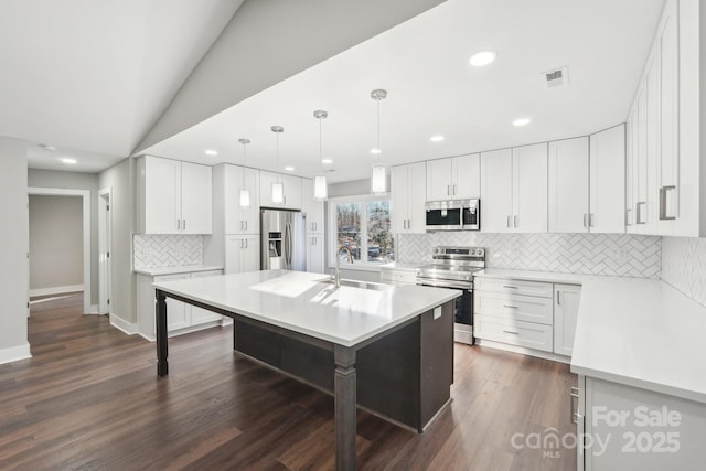 kitchen with sink, appliances with stainless steel finishes, white cabinets, a center island with sink, and decorative light fixtures