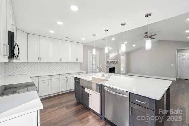 kitchen featuring appliances with stainless steel finishes, a fireplace, an island with sink, sink, and white cabinets