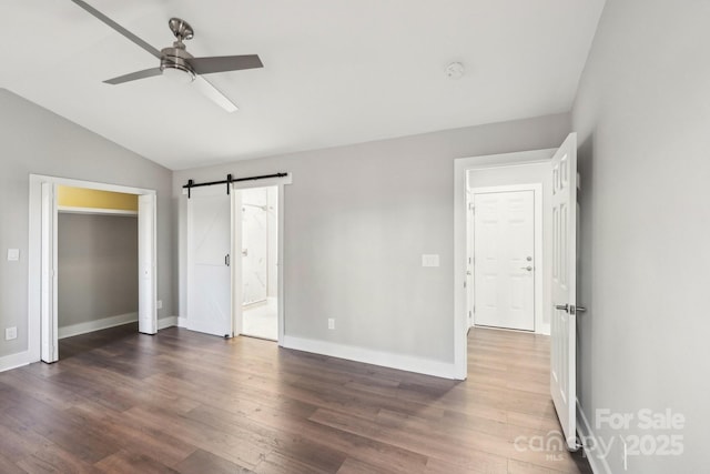 unfurnished bedroom featuring vaulted ceiling, a barn door, dark wood-type flooring, and connected bathroom