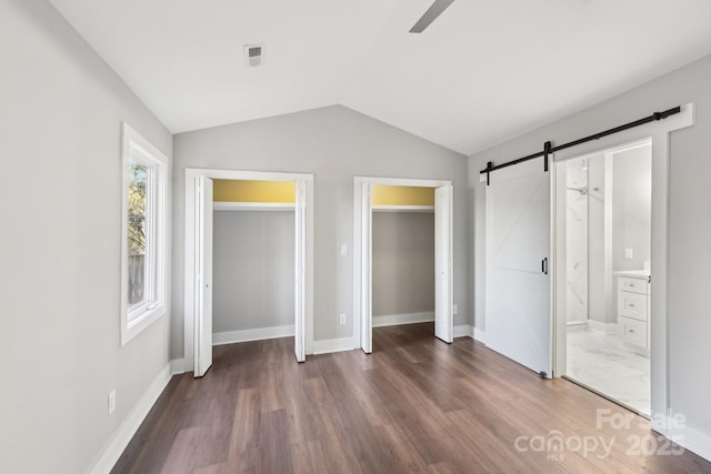 unfurnished bedroom with vaulted ceiling, a barn door, ensuite bathroom, and dark hardwood / wood-style flooring