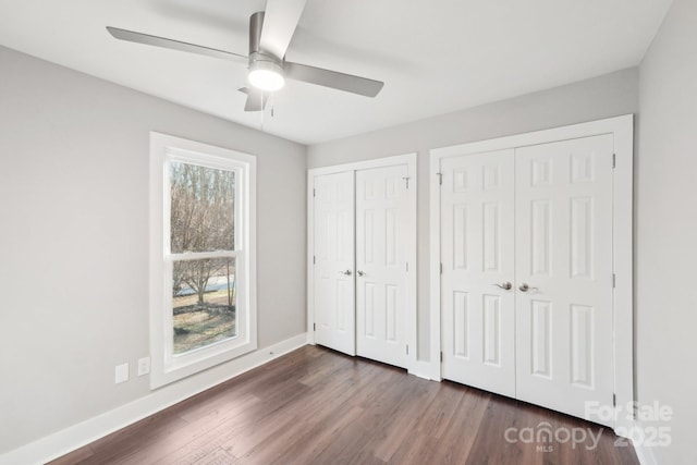 unfurnished bedroom featuring multiple windows, ceiling fan, dark hardwood / wood-style flooring, and multiple closets