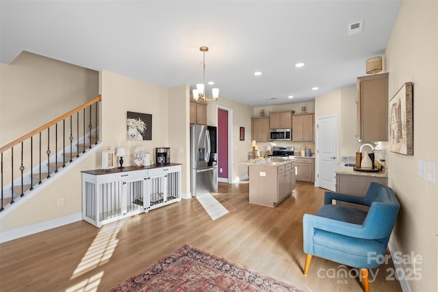 kitchen with appliances with stainless steel finishes, light hardwood / wood-style floors, a kitchen island, decorative light fixtures, and light brown cabinets