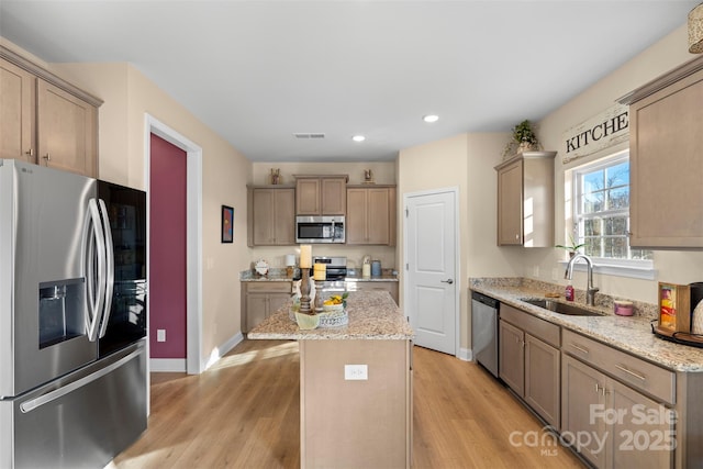 kitchen with appliances with stainless steel finishes, sink, a center island, light stone counters, and light hardwood / wood-style flooring