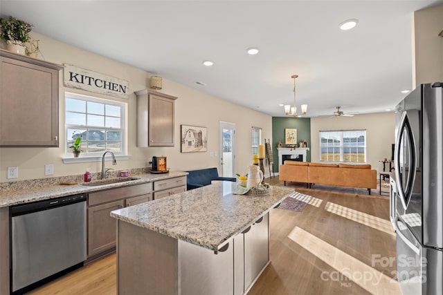 kitchen with sink, hanging light fixtures, a center island, light stone counters, and stainless steel appliances