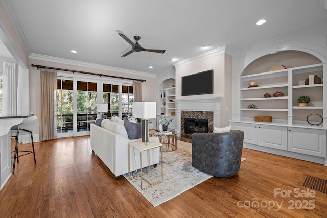 living room with crown molding, hardwood / wood-style flooring, built in features, ceiling fan, and a fireplace