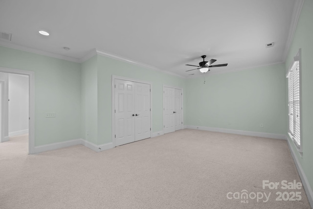 unfurnished bedroom featuring light carpet, crown molding, ceiling fan, and two closets