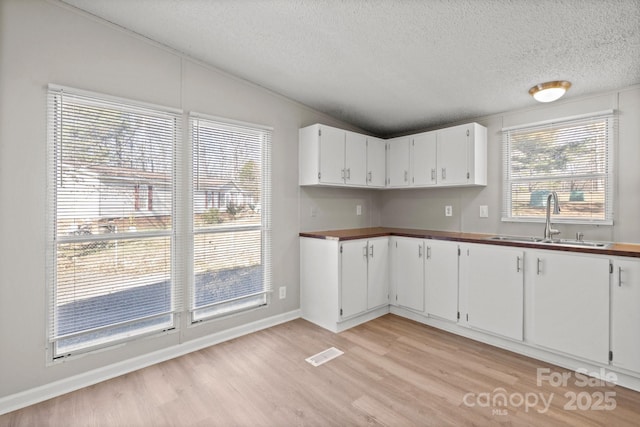 kitchen featuring a healthy amount of sunlight, sink, light hardwood / wood-style flooring, and white cabinets