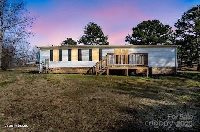 back house at dusk with a deck and a lawn