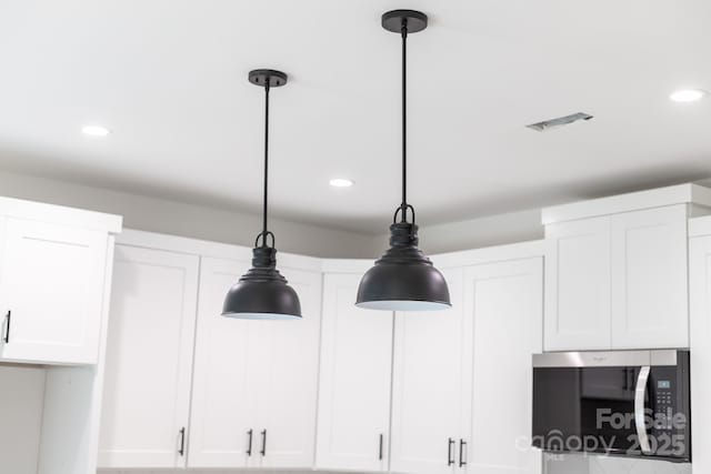details with hanging light fixtures, white cabinetry, stainless steel microwave, and recessed lighting