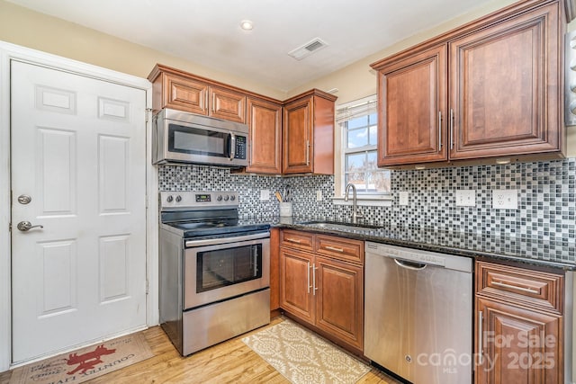 kitchen featuring sink, appliances with stainless steel finishes, dark stone countertops, tasteful backsplash, and light hardwood / wood-style floors