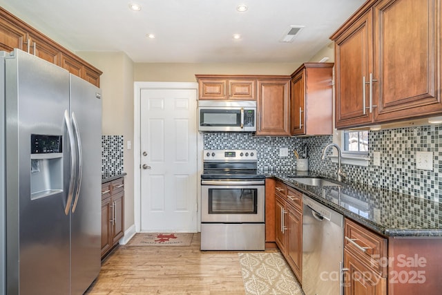 kitchen with sink, dark stone countertops, stainless steel appliances, light hardwood / wood-style floors, and decorative backsplash