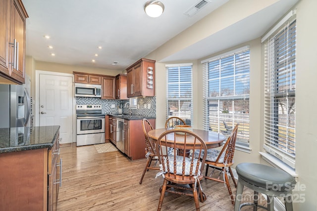 kitchen featuring sink, light hardwood / wood-style flooring, dark stone countertops, stainless steel appliances, and decorative backsplash