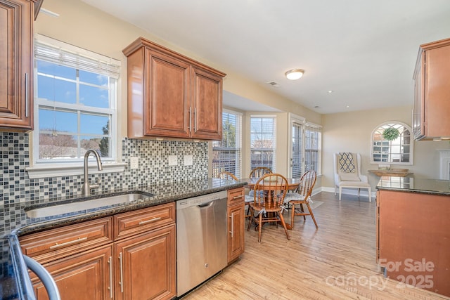 kitchen with sink, dark stone countertops, backsplash, stainless steel dishwasher, and light hardwood / wood-style flooring