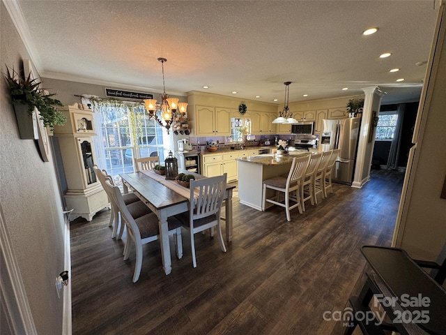 dining room featuring dark wood-type flooring, sink, ornate columns, a textured ceiling, and ornamental molding