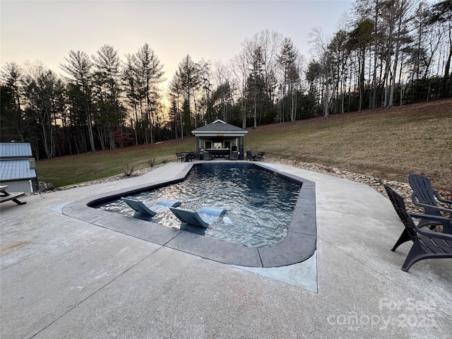 pool at dusk featuring a gazebo, a patio area, and a lawn