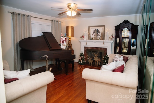 living area with ceiling fan, ornamental molding, wood-type flooring, and a brick fireplace