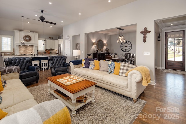 living room featuring crown molding, lofted ceiling, ceiling fan with notable chandelier, and dark hardwood / wood-style flooring