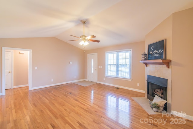 unfurnished living room with vaulted ceiling, a tile fireplace, ceiling fan, and light wood-type flooring