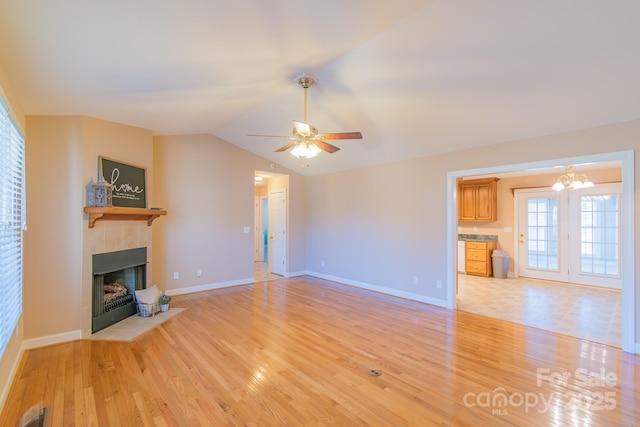 unfurnished living room with vaulted ceiling, ceiling fan with notable chandelier, a fireplace, and light hardwood / wood-style floors