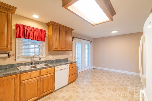 kitchen with white appliances, brown cabinetry, dark countertops, and a sink