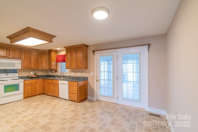 kitchen with dark countertops, white appliances, baseboards, and a sink