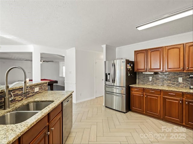 kitchen with sink, appliances with stainless steel finishes, light stone countertops, a textured ceiling, and decorative backsplash