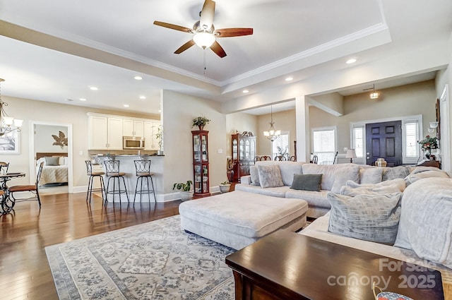 living room with ornamental molding, dark hardwood / wood-style floors, a raised ceiling, and ceiling fan with notable chandelier