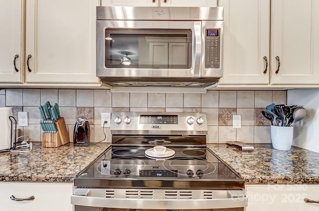 kitchen with dark stone countertops, backsplash, white cabinetry, and stainless steel appliances