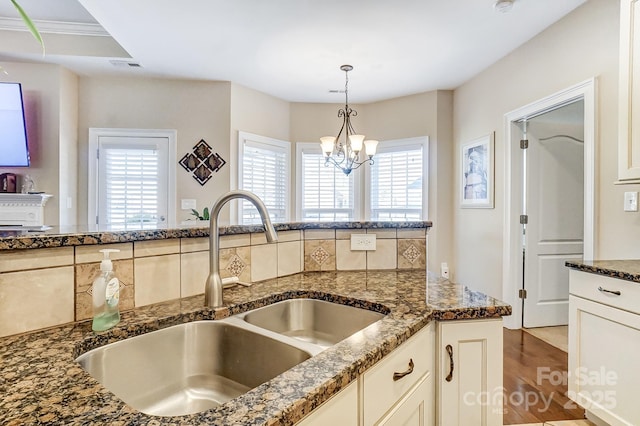 kitchen with sink, decorative backsplash, a notable chandelier, and dark stone counters