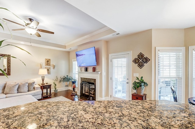 living room with dark hardwood / wood-style floors, a tray ceiling, ceiling fan, a high end fireplace, and crown molding