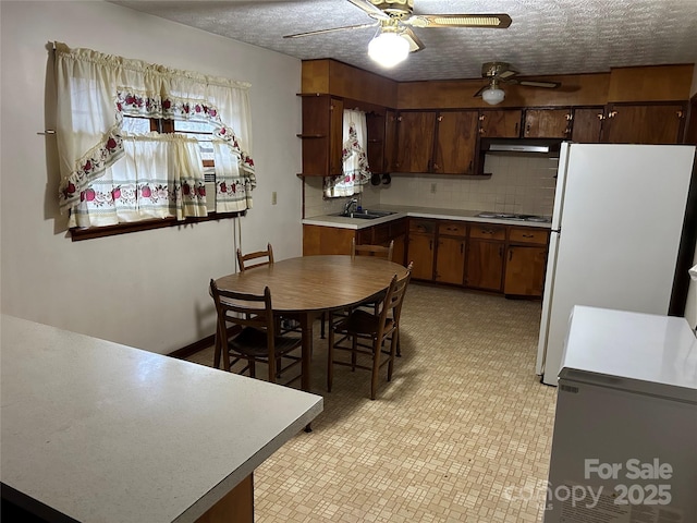 kitchen featuring sink, backsplash, stainless steel gas cooktop, a textured ceiling, and white fridge