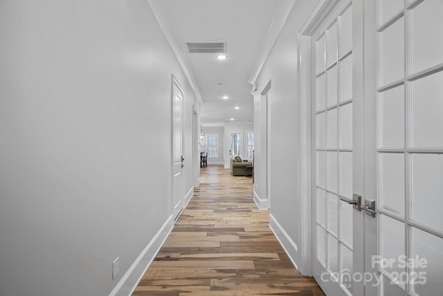 corridor with ornamental molding and light hardwood / wood-style flooring