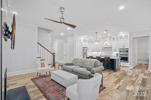 living room featuring sink, light hardwood / wood-style flooring, ornamental molding, and ceiling fan