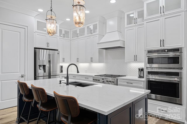 kitchen with white cabinetry, appliances with stainless steel finishes, an island with sink, and custom range hood