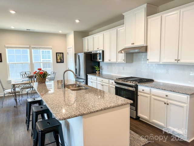 kitchen featuring sink, white cabinetry, stainless steel appliances, light stone counters, and an island with sink