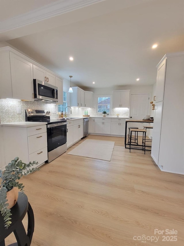 kitchen with sink, light wood-type flooring, pendant lighting, stainless steel appliances, and white cabinets