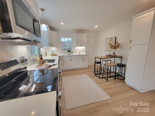 kitchen featuring white cabinetry, stainless steel appliances, decorative light fixtures, and light hardwood / wood-style flooring