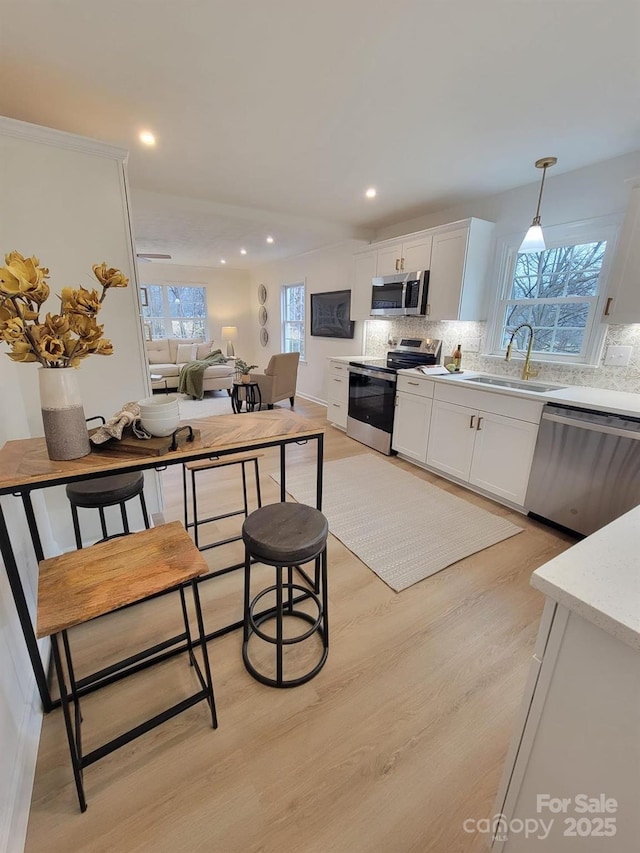 kitchen featuring stainless steel appliances, sink, white cabinets, and decorative light fixtures