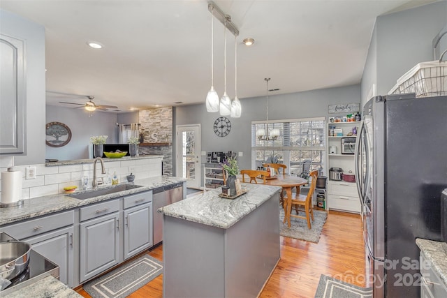 kitchen featuring decorative light fixtures, a center island, gray cabinets, stainless steel appliances, and a sink