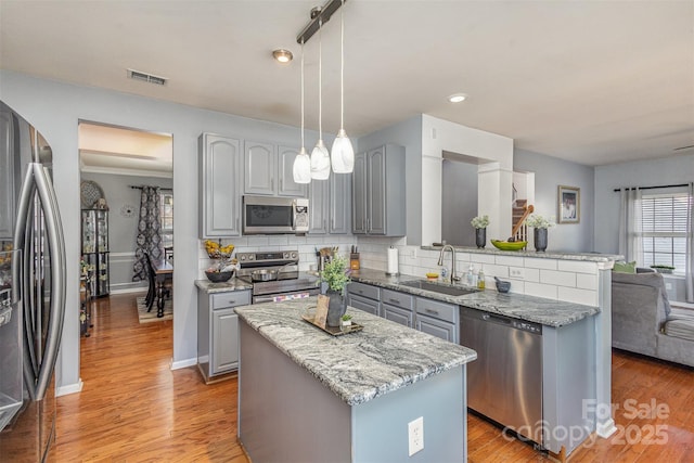 kitchen with decorative light fixtures, gray cabinets, appliances with stainless steel finishes, a kitchen island, and a sink