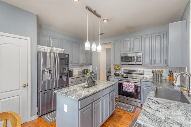 kitchen with a kitchen island, light stone counters, decorative light fixtures, stainless steel appliances, and a sink