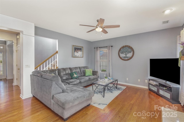 living room featuring visible vents, light wood-style flooring, a ceiling fan, baseboards, and stairs